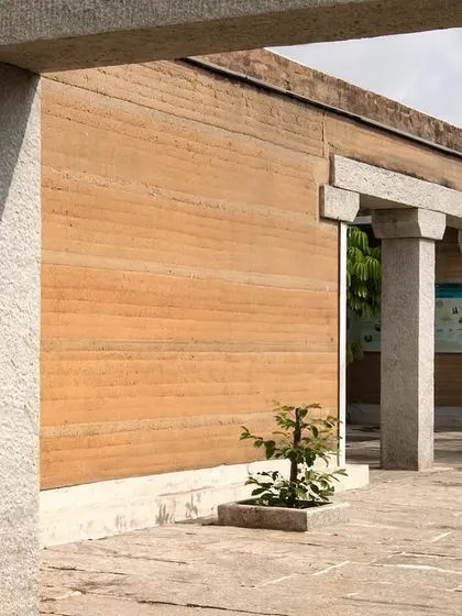 The interplay of rammed earth walls and granite stone pillars at the H.N. Science Center. This combination of two fundamental materials, earth and stone, forms the core of the building's identity.