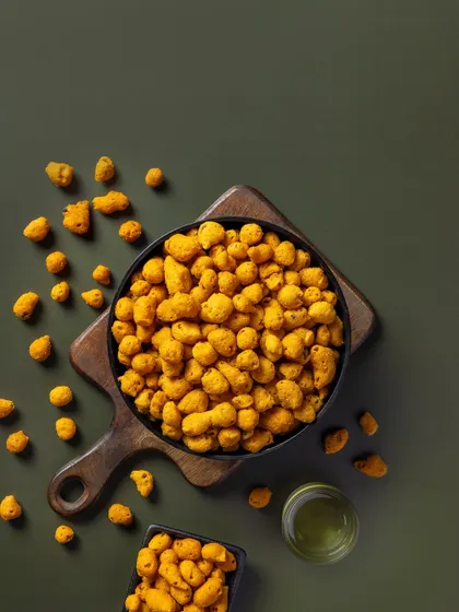 Coated peanuts against a muted green background. This composition is designed for packaging, with negative space for branding and text.