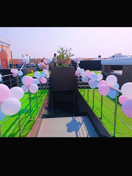 A rooftop setup for a baby shower, with pastel balloons lining the walkway on an artificial grass lawn.