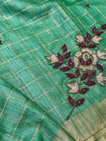 A detailed shot of the hand embroidery on the Tussar silk saree. The rich purple and white beads stand out beautifully against the green fabric.