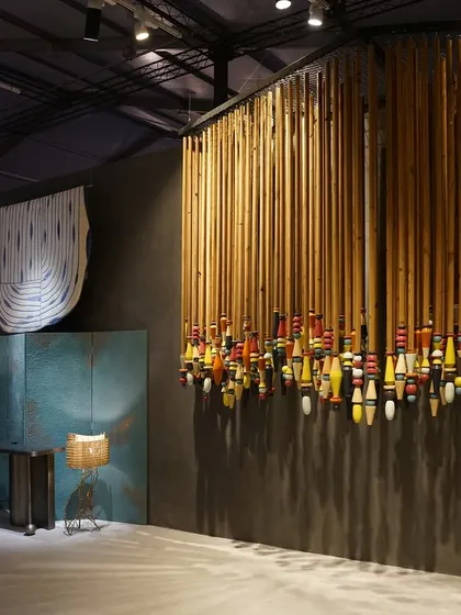 A curated view of the 'India Everywhere' space, showing a large installation of colorful lacquered wood objects from Channapatna. This piece stands in dialogue with the woven copper panels, representing India's diverse craft traditions.