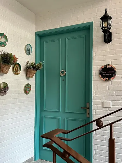 A charming entryway with a country-chic vibe. The space features a teal-colored door, a white brick wall, and decorative plates and hanging plants for a personal touch.