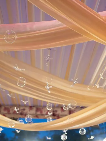 Delicate glass birds and bubbles hanging from a soft, draped canopy. These whimsical details add a touch of magic and lightness to the decor, creating a dreamy, ethereal feel for an outdoor or daytime event.