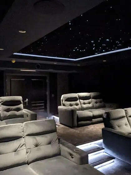 A view of a completed theater with plush grey sofas, tiered seating, and a beautiful star ceiling.