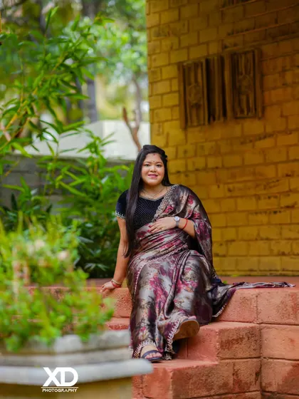 A relaxed portrait of the mother-to-be sitting on brick steps, her printed saree adding a touch of modern elegance to the rustic setting.