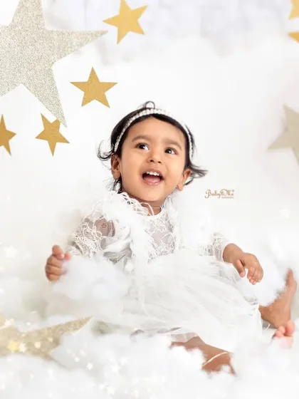 A pure, joyful laugh that lights up the photo. The all-white outfit and backdrop make the golden stars pop.