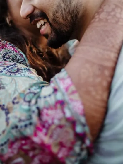 A close-up of a couple sharing a happy, intimate hug, with the focus on their smiles and the bride's mehndi.