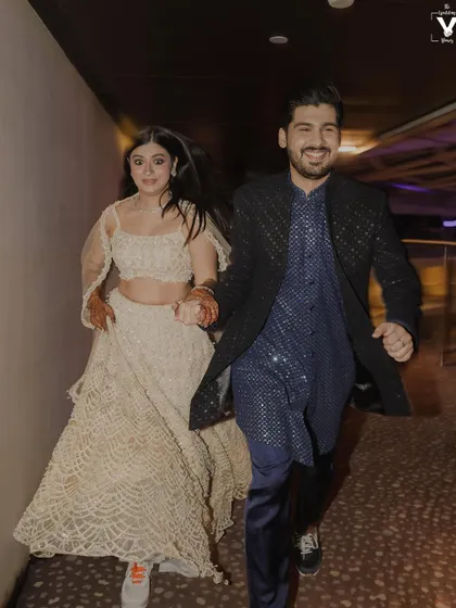 The bride and groom, in sneakers, run hand-in-hand down a corridor. This energetic and candid shot perfectly captures their fun-loving personalities and the excitement of their sangeet night.