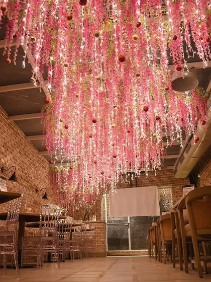 A wide view of the pink floral Christmas ceiling. The exposed brick walls provide a rustic contrast to the whimsical, glowing installation.