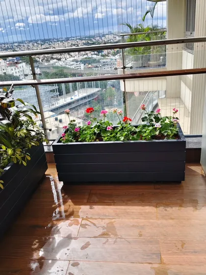A planter box filled with pink and red geraniums, adding a pop of color to this city balcony with a wide urban view.