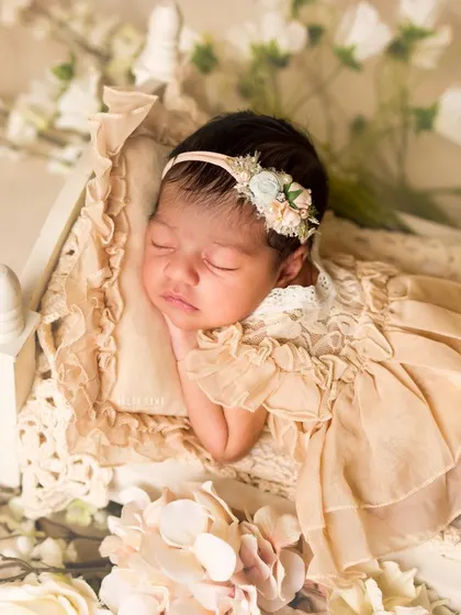Dreaming in a field of flowers. This newborn is posed so delicately on a miniature bed, surrounded by soft white and pink blossoms, creating a truly ethereal portrait.