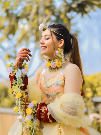 A candid portrait of the bride, smiling brightly in her yellow Haldi outfit and floral jewelry. The natural light and joyful expression make this a timeless memory.