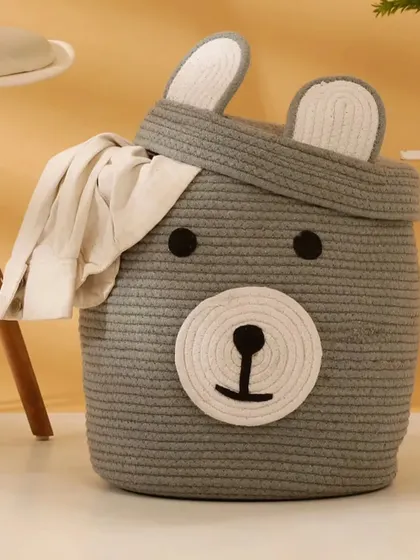 Here is the bear storage basket in a lovely grey color, shown holding a piece of clothing to demonstrate its use as a laundry hamper.