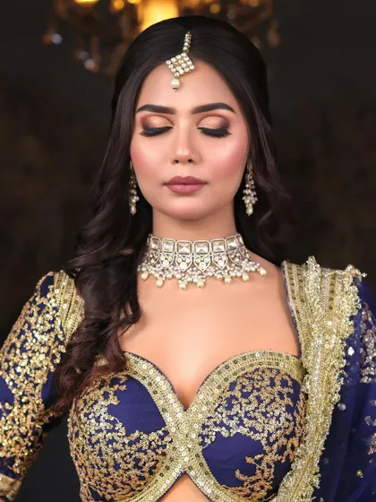 A sophisticated reception look in a royal blue and gold lehenga. The makeup is kept classic with a brown smokey eye and soft waves.