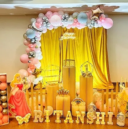 A charming Disney Princess themed birthday decoration. The setup includes cutouts of Princess Aurora and Snow White, a golden backdrop, and a pink and silver balloon arch for a royal celebration.