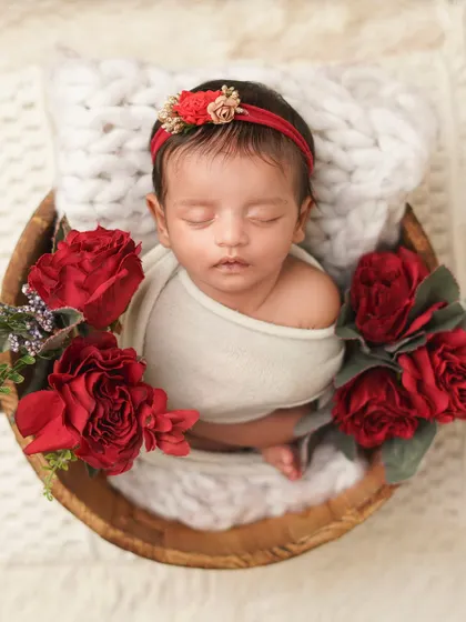 An overhead shot of a newborn in a wooden bowl, surrounded by rich red roses. This setup creates a romantic and classic feel for a baby girl's first photoshoot.