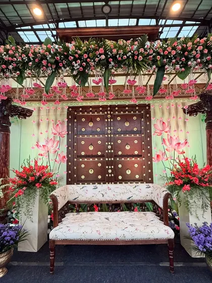 A stunning engagement stage with a Pichwai theme. The hand-painted backdrop, traditional wooden pillars, and lotus flower hangings create a rich, artistic look.