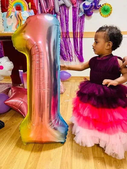 The younger sister celebrating her first birthday in a smaller version of the same colorful tiered gown.