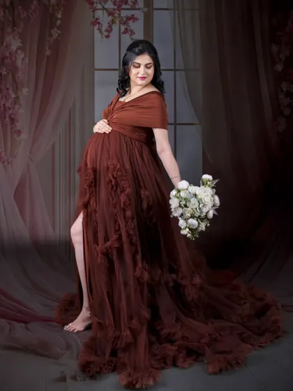 An elegant standing portrait against a soft, draped background. The mom-to-be holds a bouquet, and the lighting creates a gentle, romantic mood.