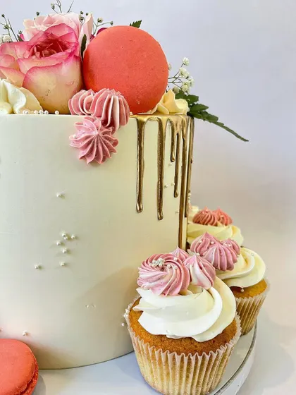 A closer look at the details on this floral drip cake. You can see the delicate gold drip, the piped buttercream swirls, and the perfectly coordinated cupcakes that sit alongside the main cake, creating a cohesive dessert display.