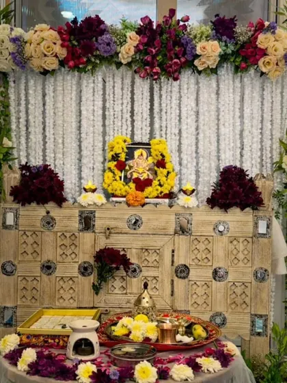I designed this serene pooja corner for a client's home. The setup features a backdrop of delicate white rajnigandha strings, complemented by a lush arrangement of cream roses and deep purple flowers on a rustic wooden cabinet.