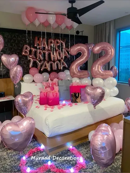 Our pink and rose gold themed bedroom decorations are a popular choice for birthdays. This surprise setup includes large number balloons, "Happy Birthday" foil letters, and a bed filled with heart-shaped balloons and gifts.