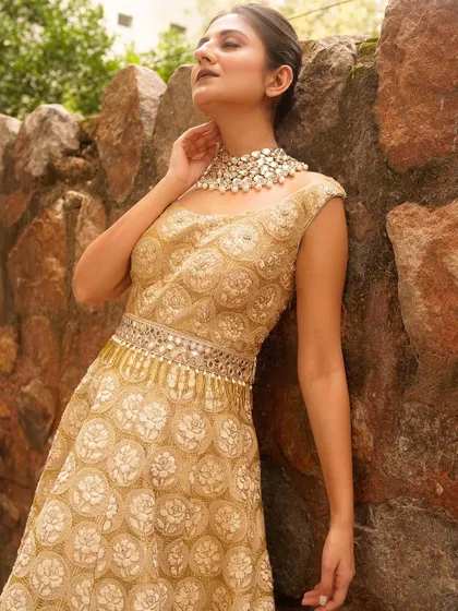 A sun-kissed shot highlighting the exquisite pearl necklace and the detailed embroidery on the golden gown. The model's pose exudes a sense of serene luxury, perfect for a high-end ethnic wear brand.