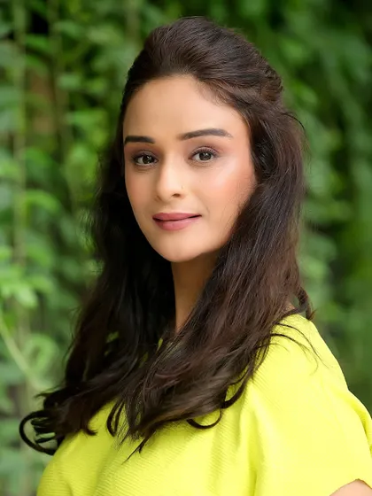 A natural outdoor headshot of Harleen Kaur. The soft, diffused light from the foliage creates a beautiful, gentle look.