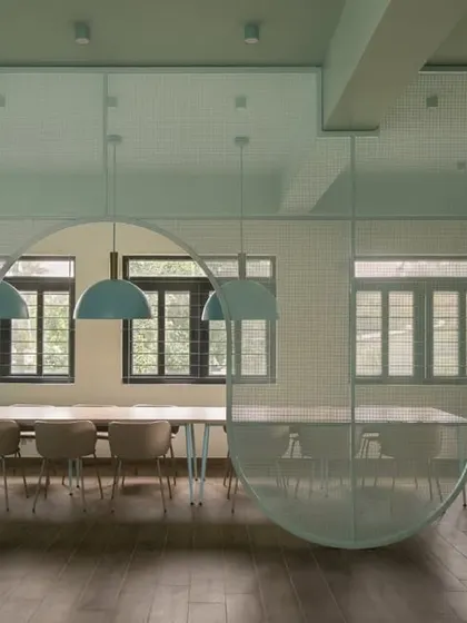 This staff dining area features a translucent, curved partition that creates a sense of separation without closing off the space. The soft green palette and simple wooden furniture create a calming atmosphere for teachers to recharge.