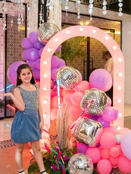 A beautiful photo opportunity with a light-up arch and a cascade of pink and purple balloons mixed with disco balls.