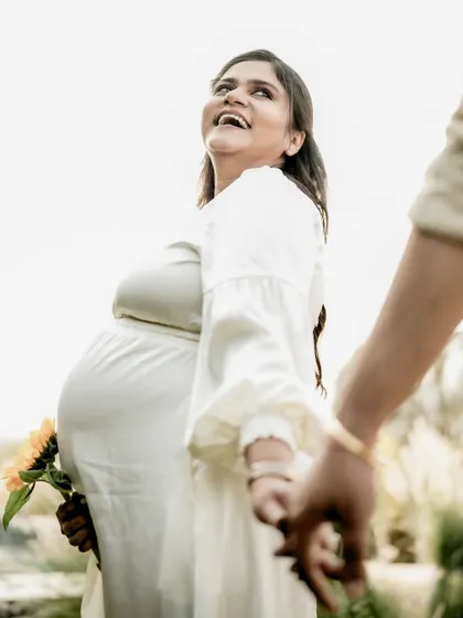 A joyful "follow me" shot, with the mom-to-be in a flowing white dress, laughing as she leads her partner.