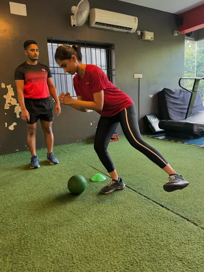 A coach guides a client through a single-leg balance drill with a medicine ball, improving stability and proprioception.