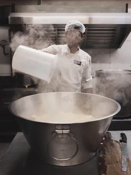A chef works over a large vat, surrounded by steam. This is the heart of our cheese kitchen, where the transformation from milk to cheese happens every day.