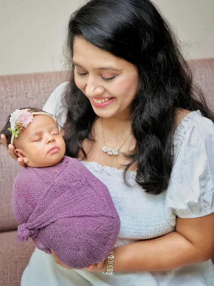 A mother's gentle smile as she holds her sleeping newborn. The soft lighting and simple background keep the focus on this beautiful, quiet moment.