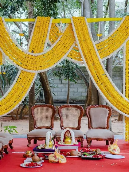 A traditional Varapooja setup, with a backdrop of draped marigold garlands and grand golden pillars, creating a sacred and regal atmosphere.