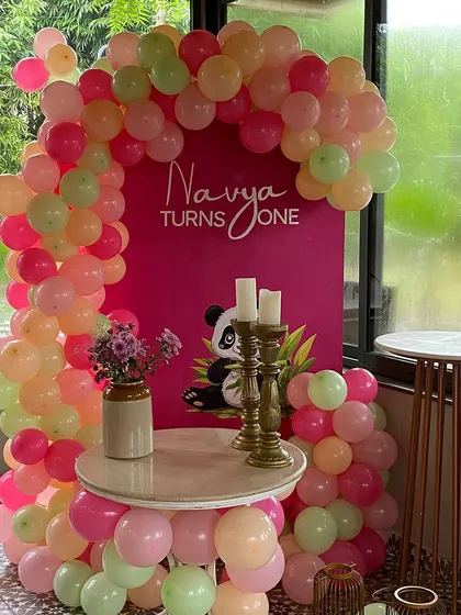 A chic first birthday corner with a balloon arch in shades of pink, peach, and mint green. The custom backdrop features a cute panda graphic for a modern and sweet touch.