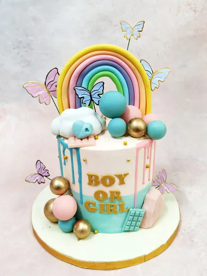 We celebrate new arrivals with this playful and modern gender reveal cake. Drips of pink and blue cascade down the side, while a vibrant rainbow, whimsical butterflies, and decorative spheres in gold, pink, and blue add to the joyful anticipation of discovering if it is a boy or a girl.