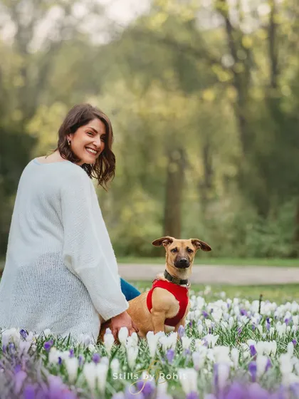 A joyful, candid moment captured among a field of spring crocuses. Her smile and the dog's curious expression perfectly embody the fresh, happy feeling of a spring day in the park.