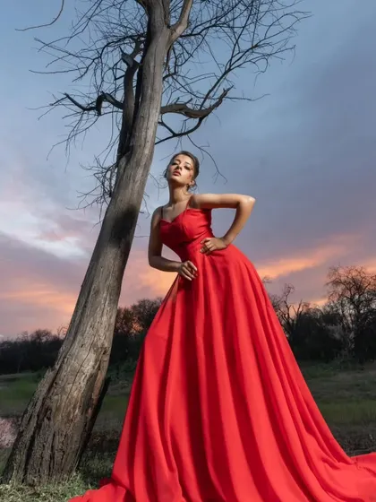 A powerful and striking pose. The vibrant red gown stands out beautifully against the dramatic sunset sky, creating a truly artistic and memorable pre-wedding shot.