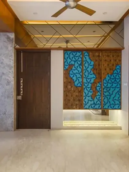 The modern living room foyer in J House features a bold blue-and-brown geometric feature wall. Mirrored ceilings and a metallic tree installation elevate the contemporary design while preserving fluidity between spaces.