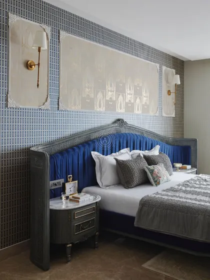 This bedroom features a striking royal blue pleated headboard against a patterned grey wallpaper. The custom artwork above the bed was designed to complement the room's classic yet modern aesthetic.