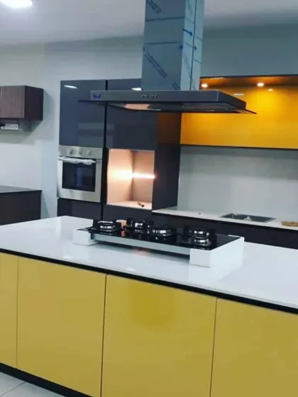A bold and contemporary kitchen design featuring a bright yellow island with a built-in hob. The island is contrasted with dark grey tall units and a yellow-accented backsplash, creating a vibrant focal point.