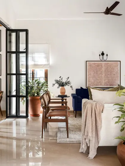 This living room is designed to be a tranquil oasis. The soothing color palette, plush cushions, and abundance of green plants create a sanctuary for unwinding and relaxation. The pop of blue from the sofa adds a touch of sophisticated color.
