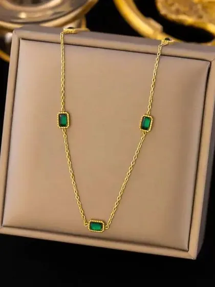A delicate gold-toned chain necklace adorned with small, rectangular emerald-green stones. This piece adds a subtle pop of color and is perfect for layering or wearing on its own.