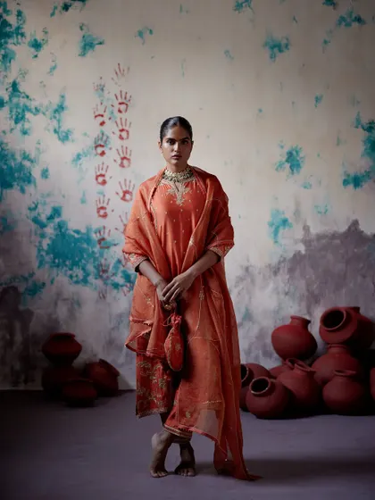 An earthy orange kurta set with a matching potli bag. The intricate embroidery and rich colour make it a warm and inviting choice for any festive gathering.