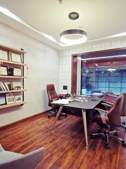 A view into the director's office, showing the use of warm wood flooring and a minimalist shelving unit for displaying awards. The glass partition maintains a connection to the rest of the office while ensuring privacy.