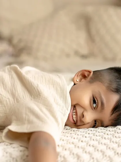 A young boy lies on a bed with a playful, sideways glance at the camera. This candid shot captures a moment of pure, childlike fun.