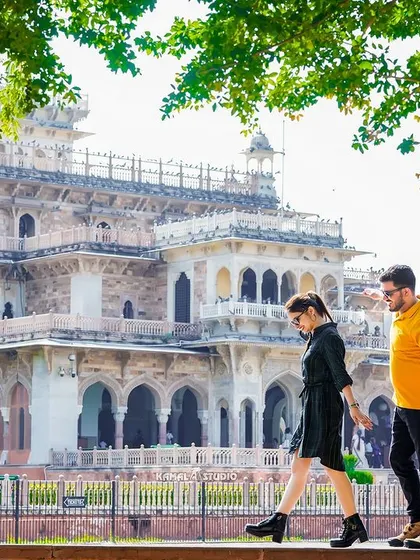 A stylish, candid shot of the couple walking along a wall with the Albert Hall Museum in the background, showcasing a modern, casual vibe in a historic setting.