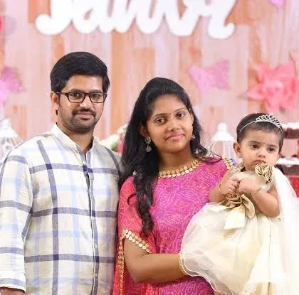 A family of three poses in front of a beautifully decorated dessert table at their daughter's event.