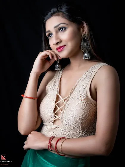 A studio portrait against a black background, focusing on the model's radiant expression. She wears a lace top and large traditional earrings, blending modern and ethnic styles.